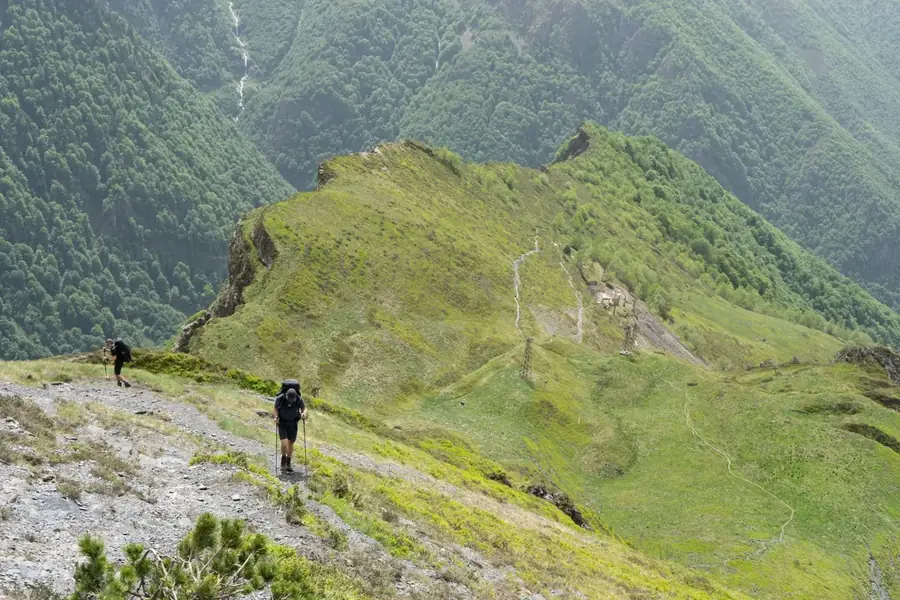 Wandelaars met trekkingrugzak klimmen een bergkam op boven een groen dal in de Val d'Aran