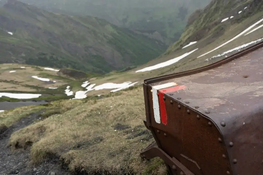 Roestige mijnwagen met rood-witte GR-markering boven een dal met sneeuwresten in de Val d'Aran