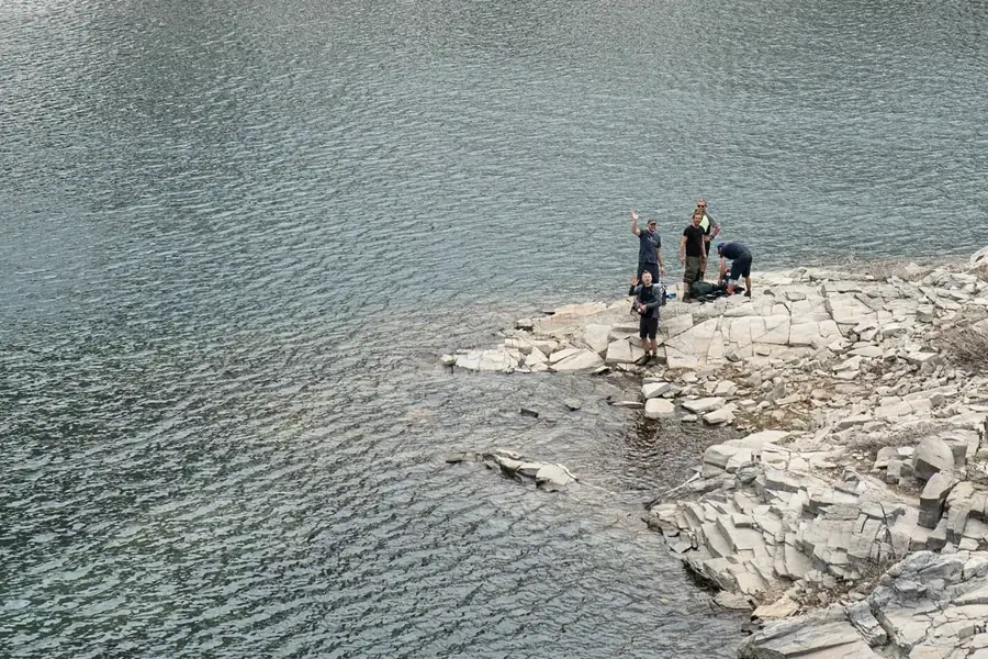 Groep wandelaars zwaait vanaf de rotsige oever van een bergmeer in de Val d'Aran