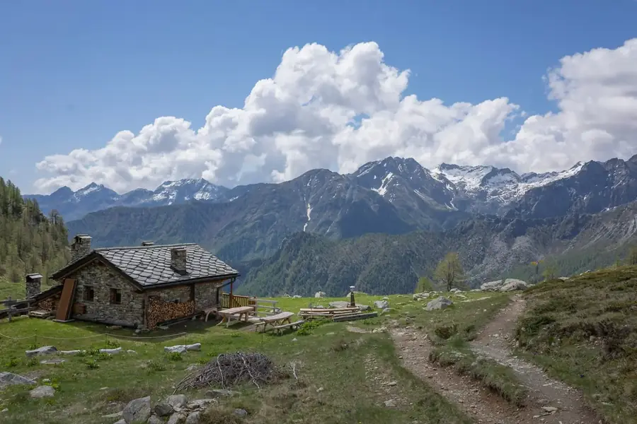 Stenen alpenhut met picknicktafels langs het wandelpad, met uitzicht op de besneeuwde Alpen